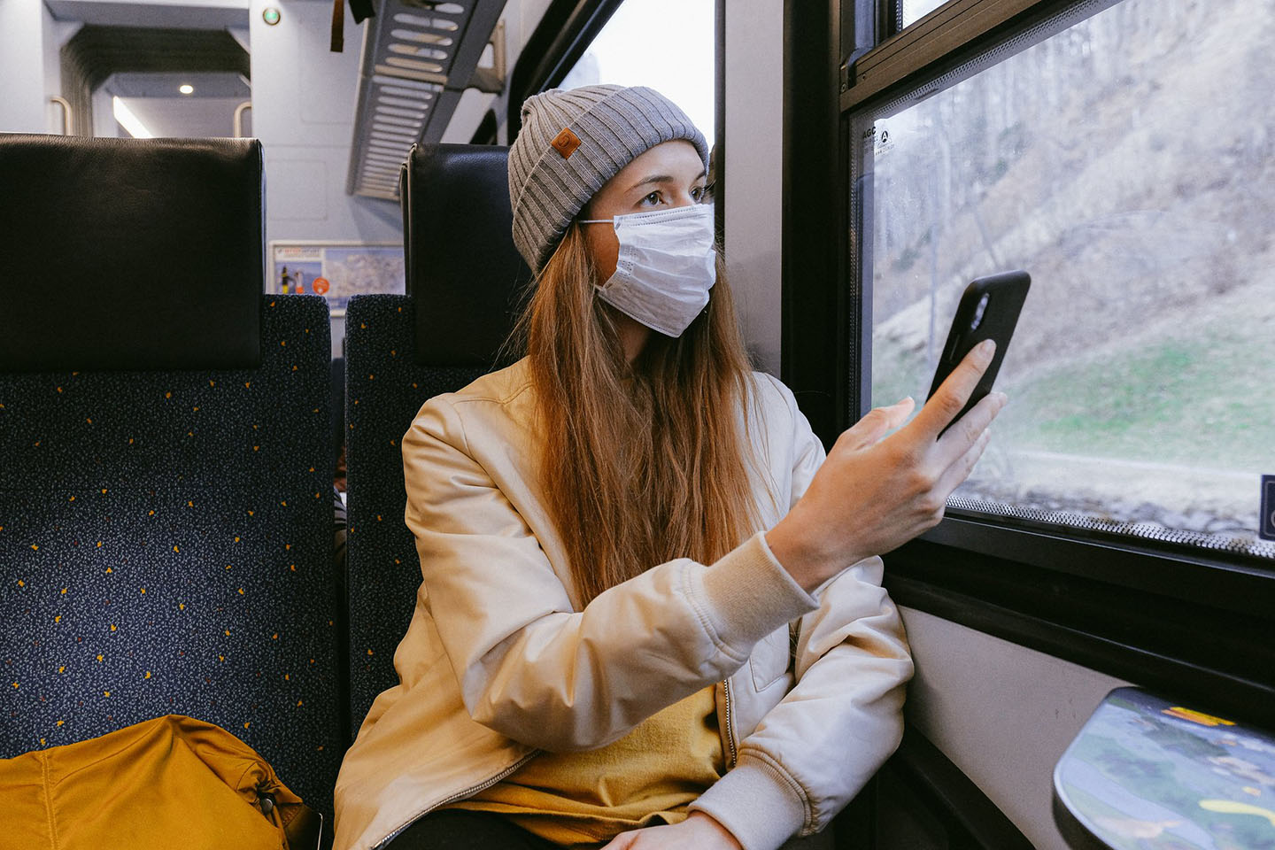 Chica usando barbijo y celular en asiento de un tren